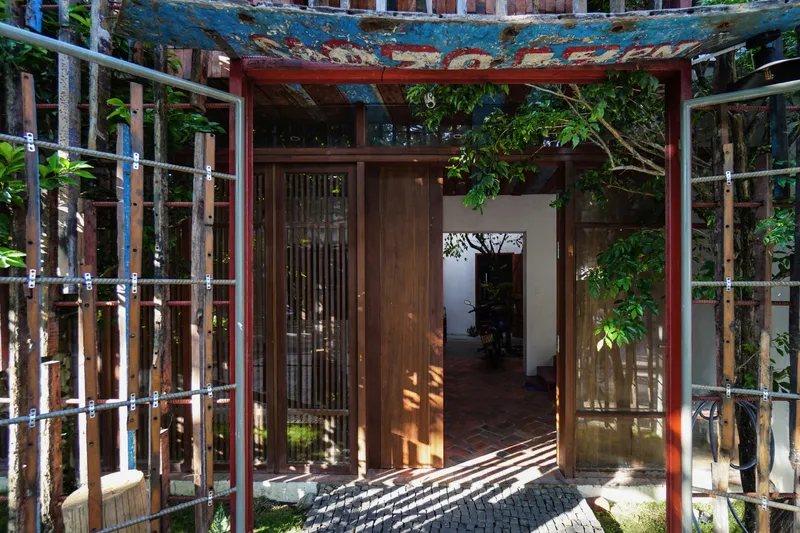 Entrance threshold with weathered timber door and salvaged blue metal canopy framing a courtyard with foliage