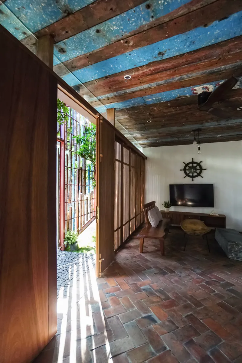 Interior room with reclaimed metal ceiling panels, herringbone brick floor and timber screen opening to garden