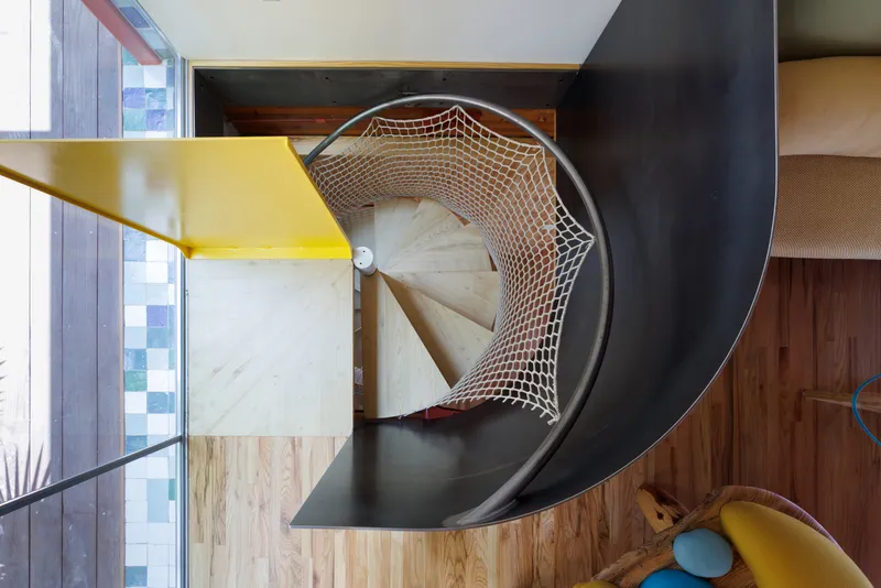 Overhead view of a curved staircase with rope netting balustrade and yellow steel handrail