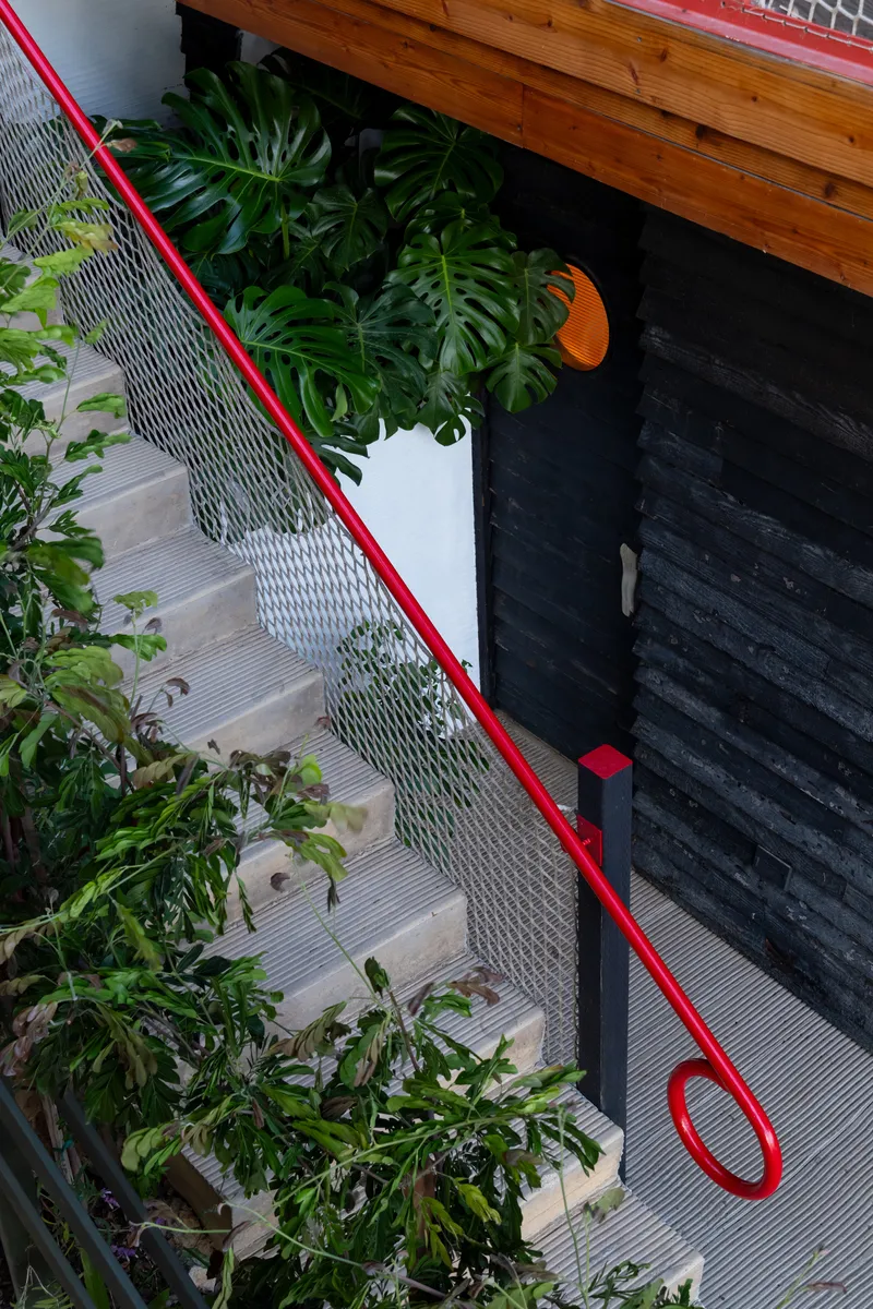 Timber staircase with red tubular steel handrail and planted beds along the wall