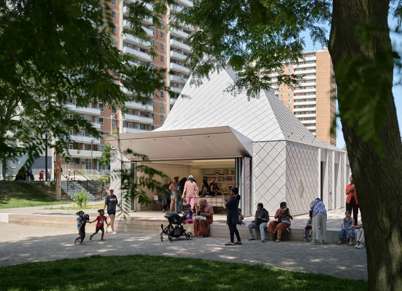 Angled view of the diamond-patterned metal facade and cantilevered canopy with families gathering in the park