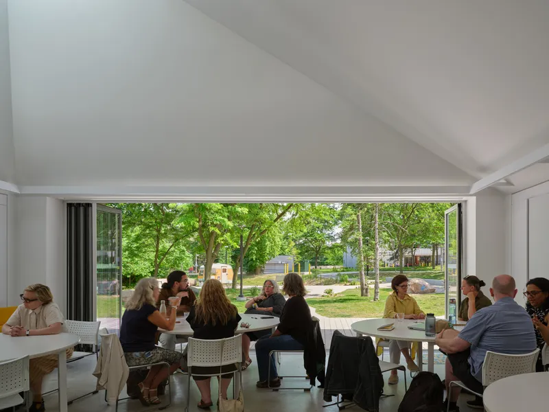 Interior room with sloped white ceiling and large window framing view of trees and park