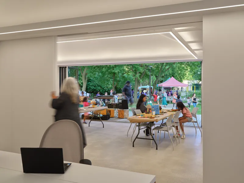 View through interior workspace showing recessed lighting coves and community activities on the outdoor deck