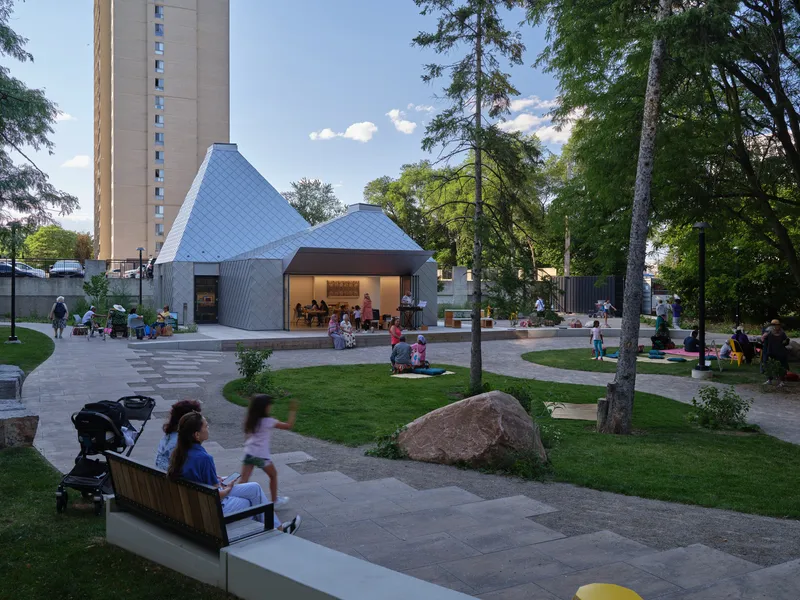 Pavilion with three peaked roofs and corrugated metal cladding set in a landscaped park at dusk
