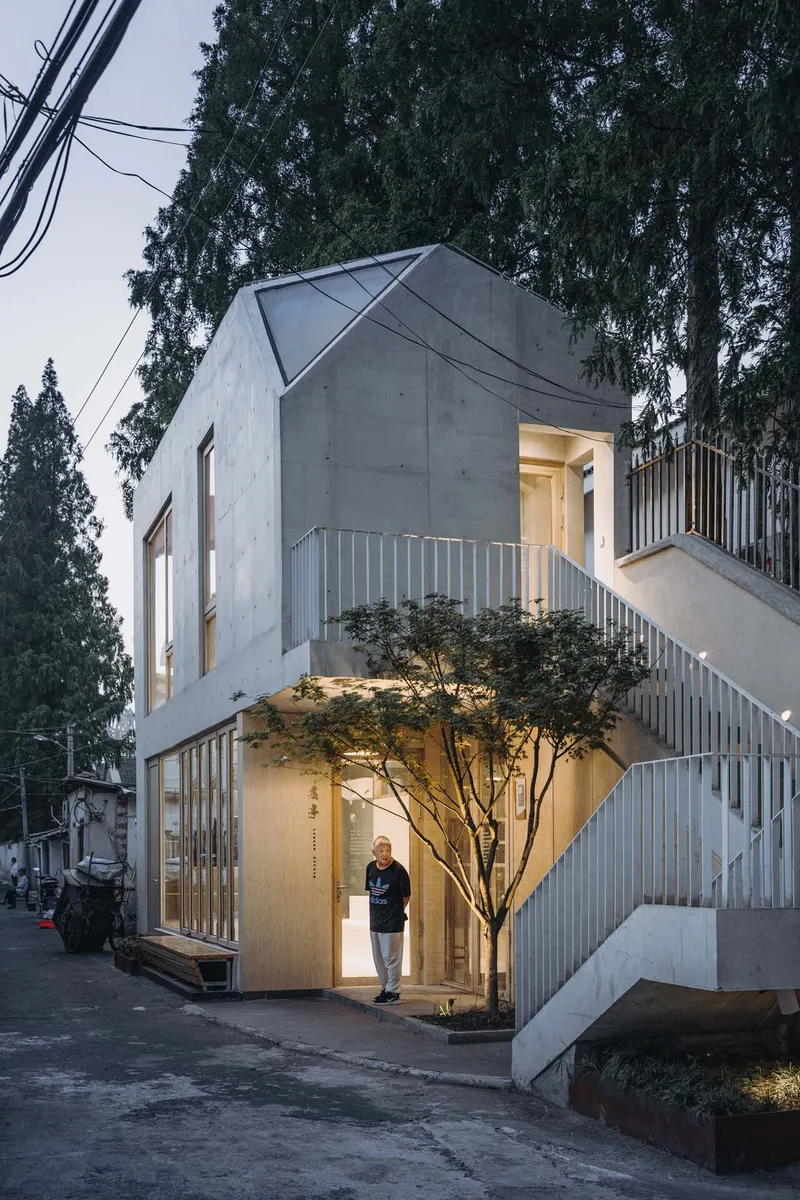 Corner facade showing the angled concrete volumes with timber screens and a resident at the entrance