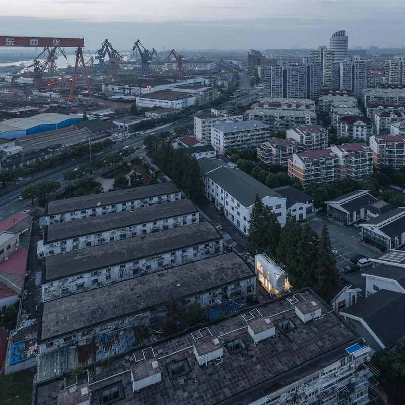 Aerial view of the compact house among warehouse rooftops and shipyard cranes at dusk