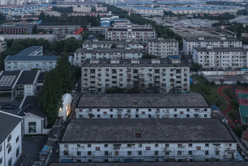 Drone view of the illuminated house nestled between residential blocks and a sports court at twilight