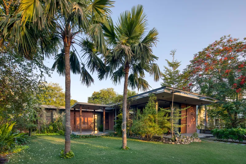 Garden view showing low-slung pavilions with overhanging roofs among palms and deciduous trees at dusk