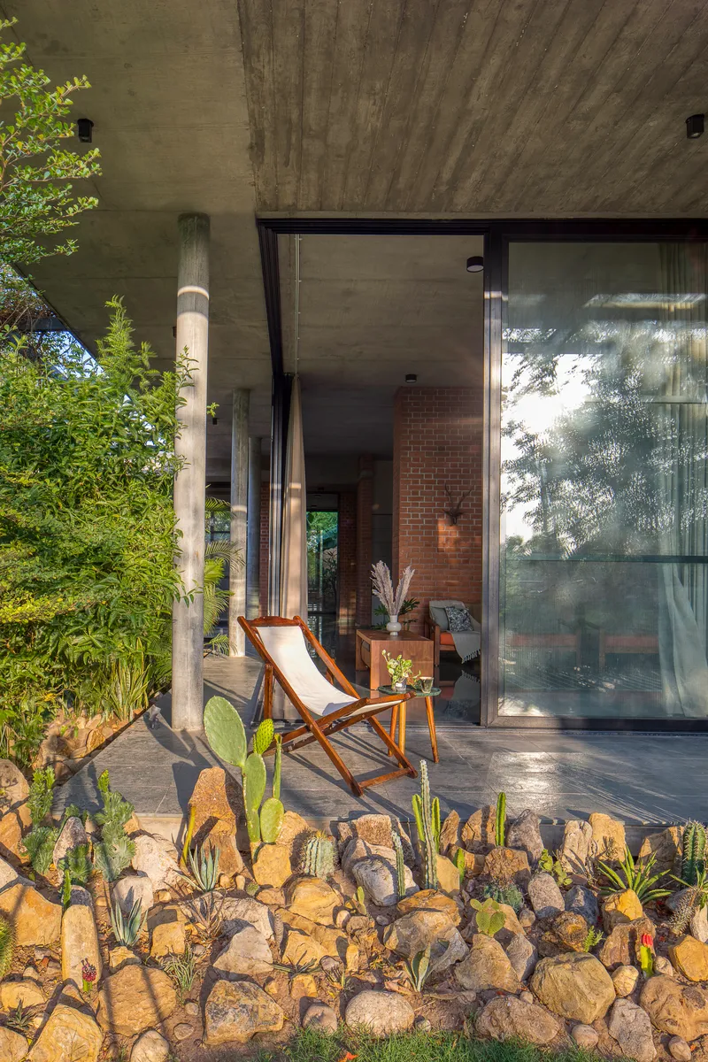Covered terrace with cylindrical concrete columns and board-formed ceiling casting dappled shadows on paving