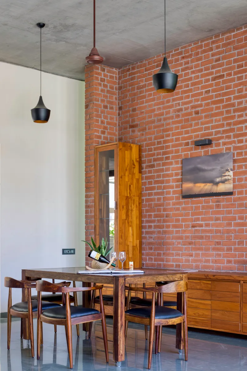 Dining area with exposed brick wall, concrete ceiling, black pendant lights, and timber furniture