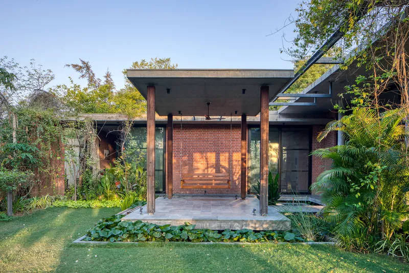 Entrance pavilion with timber columns and floating concrete roof framing a brick wall at dusk