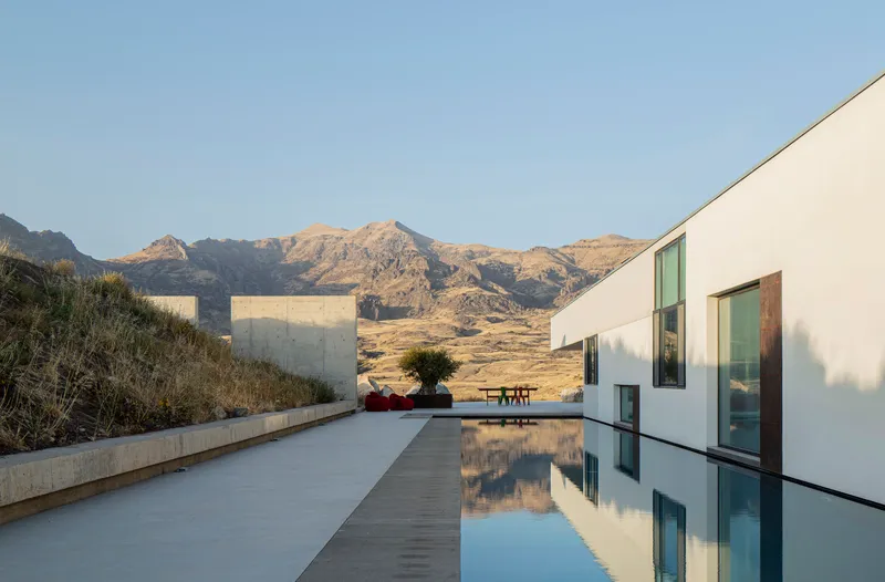 Concrete terrace with reflecting pool and white volumes framed by arid hills under evening light
