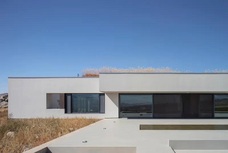 White stucco facade with horizontal windows and stepped concrete terraces against dry grasses