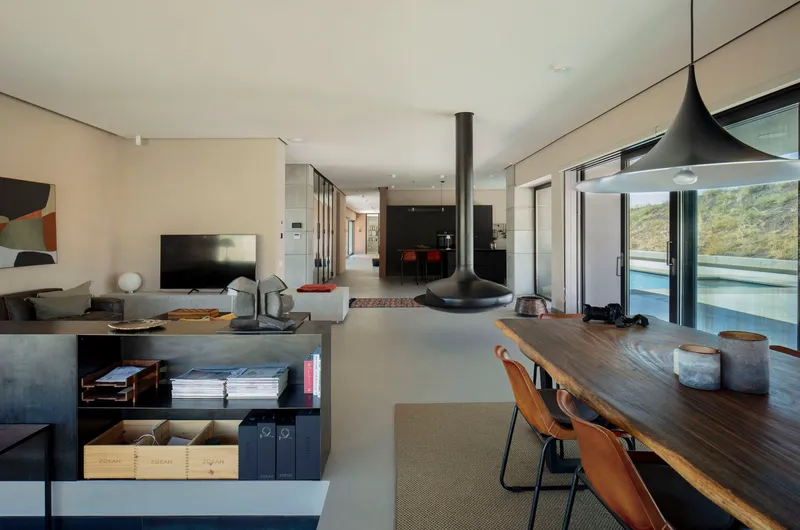 Open living space with suspended conical fireplace and timber dining table overlooking the hillside