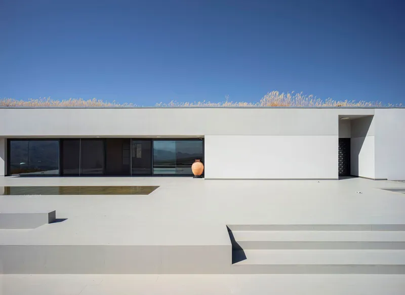 White rendered terrace with wide steps ascending to a horizontal window band under a clear blue sky