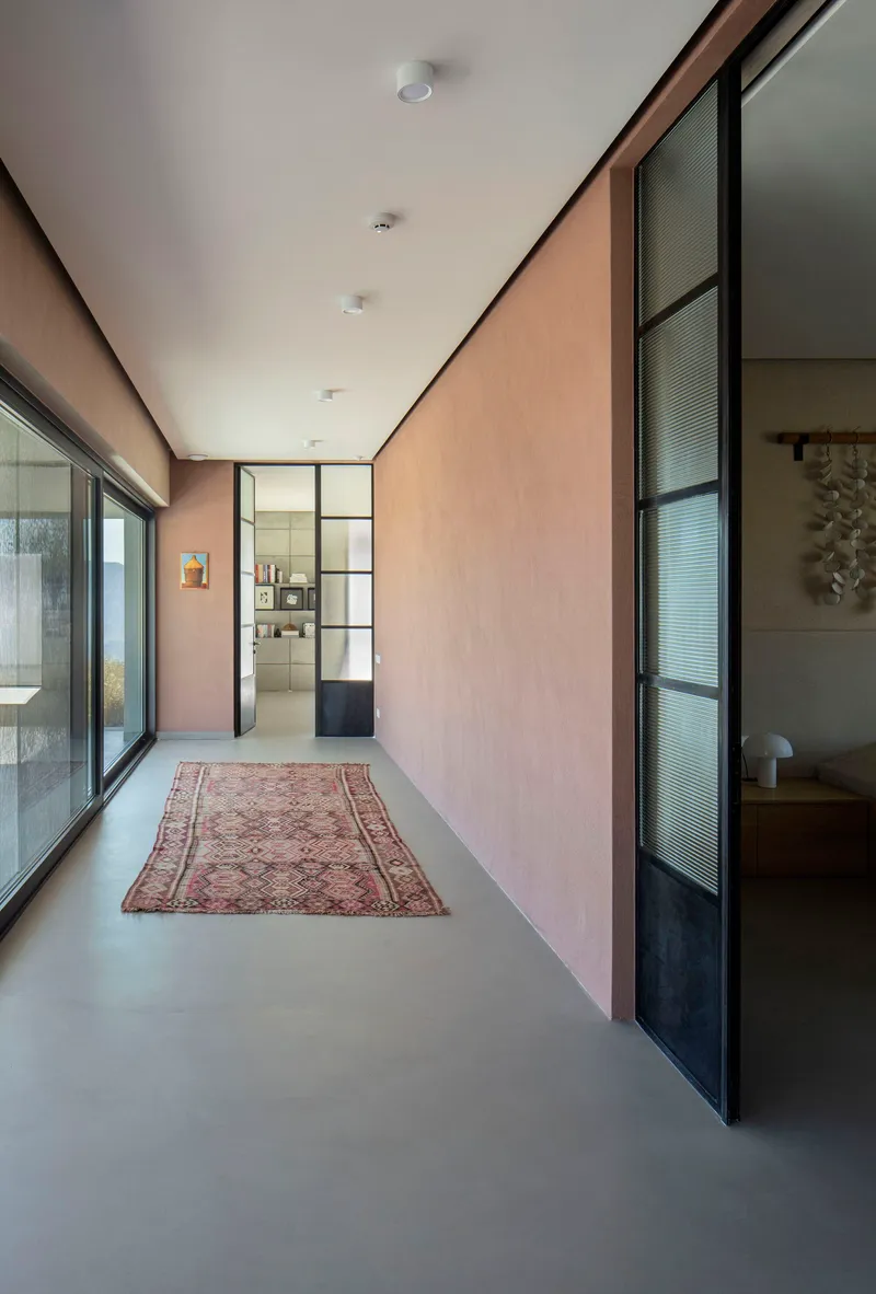 Corridor with pale plaster walls, steel-framed glass partitions, and a vintage rug on polished concrete flooring