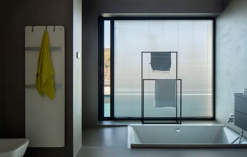 Bathroom with recessed tub beside a window fitted with translucent pleated blinds and a towel rack