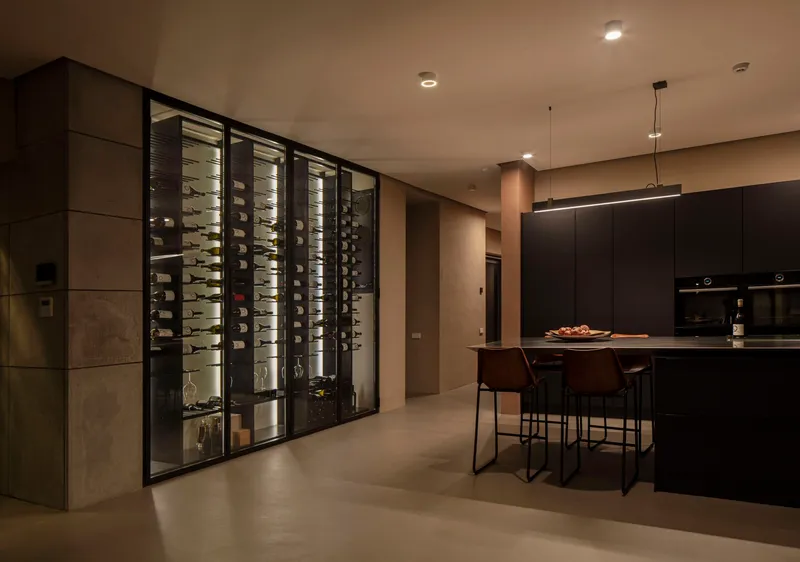 Kitchen with backlit wine storage wall and dark cabinetry under warm evening lighting