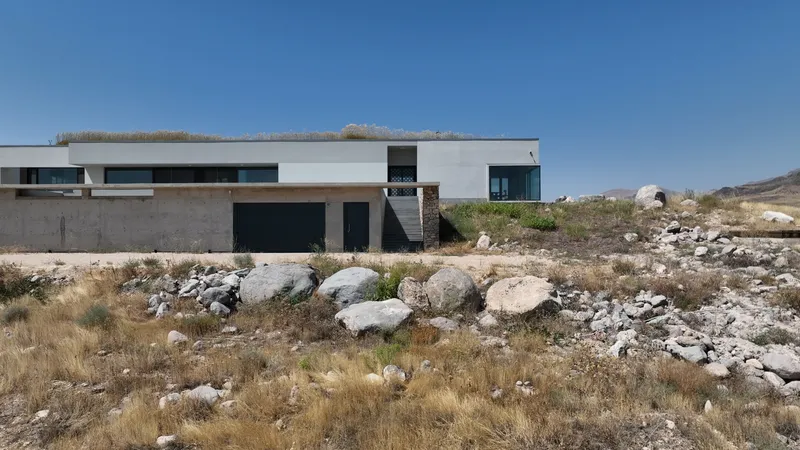 White horizontal volume with terrace roof set among rocky desert terrain under clear blue sky