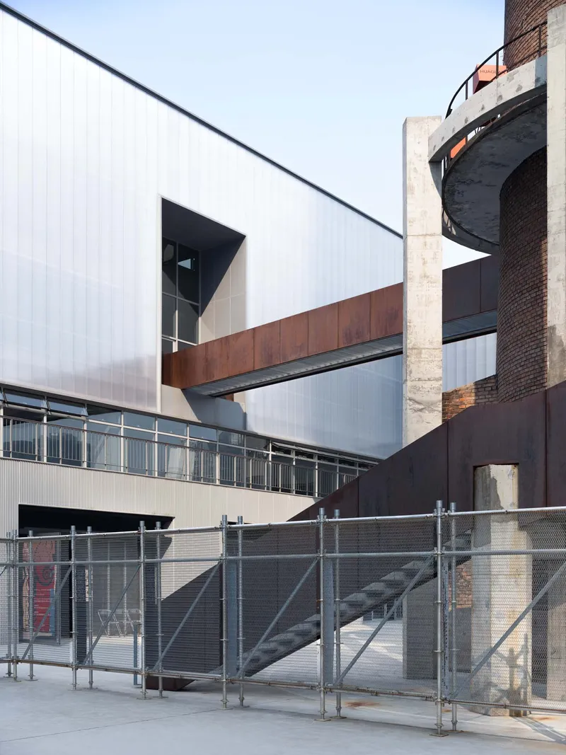 Close-up of the polycarbonate cladding meeting the weathered steel bridge and exposed concrete columns