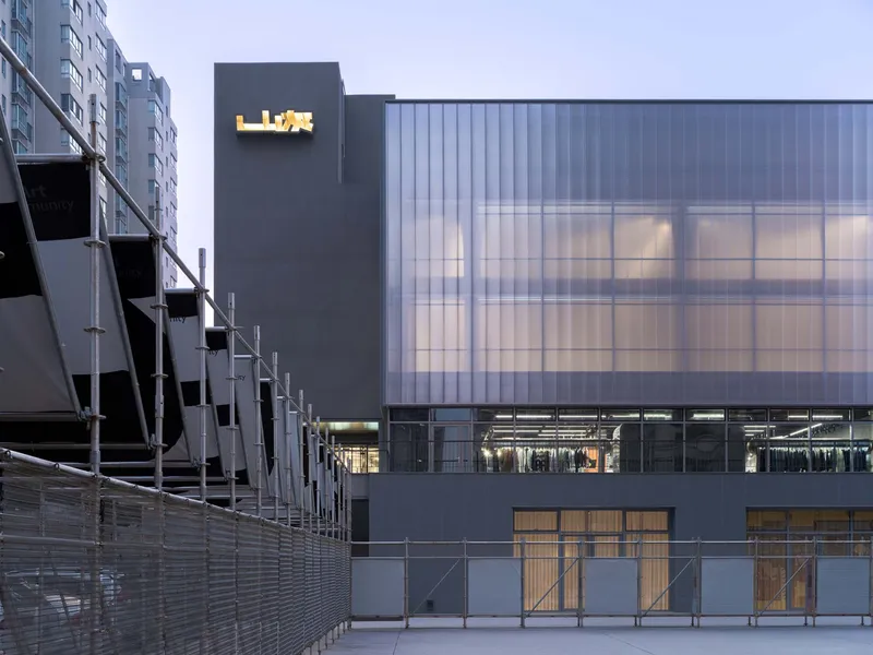 Translucent polycarbonate facade and projecting signage tower at twilight beside a residential block