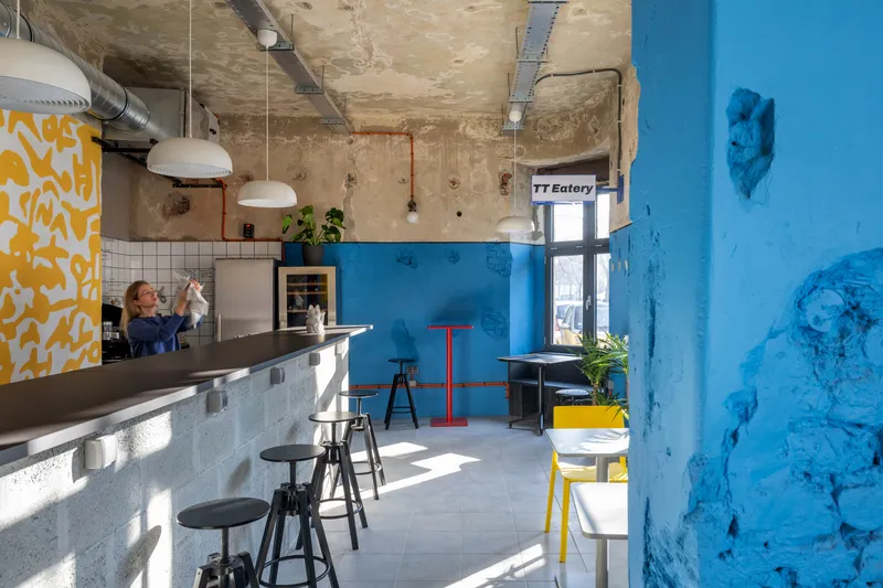 Service counter in raw concrete with white tile backsplash beneath distressed plaster ceiling and exposed ducts