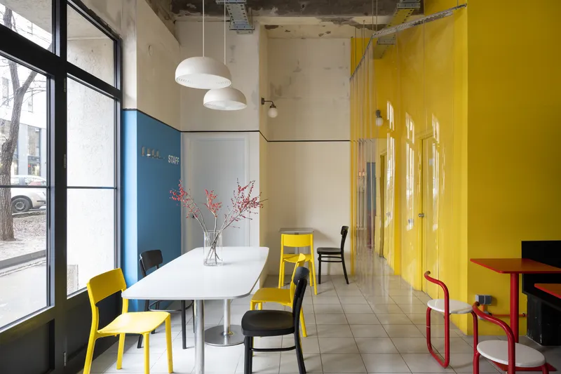 Seating area with white table and yellow translucent curtain beside blue wall and street-facing windows