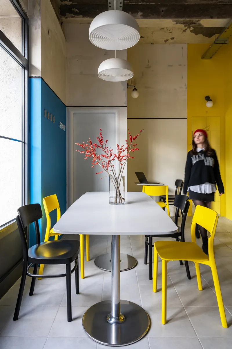 White table with vase of red branches beneath two hanging disc lights with a person passing by
