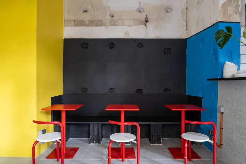Red tubular steel seating with banquette bench against black panel wall and exposed concrete above