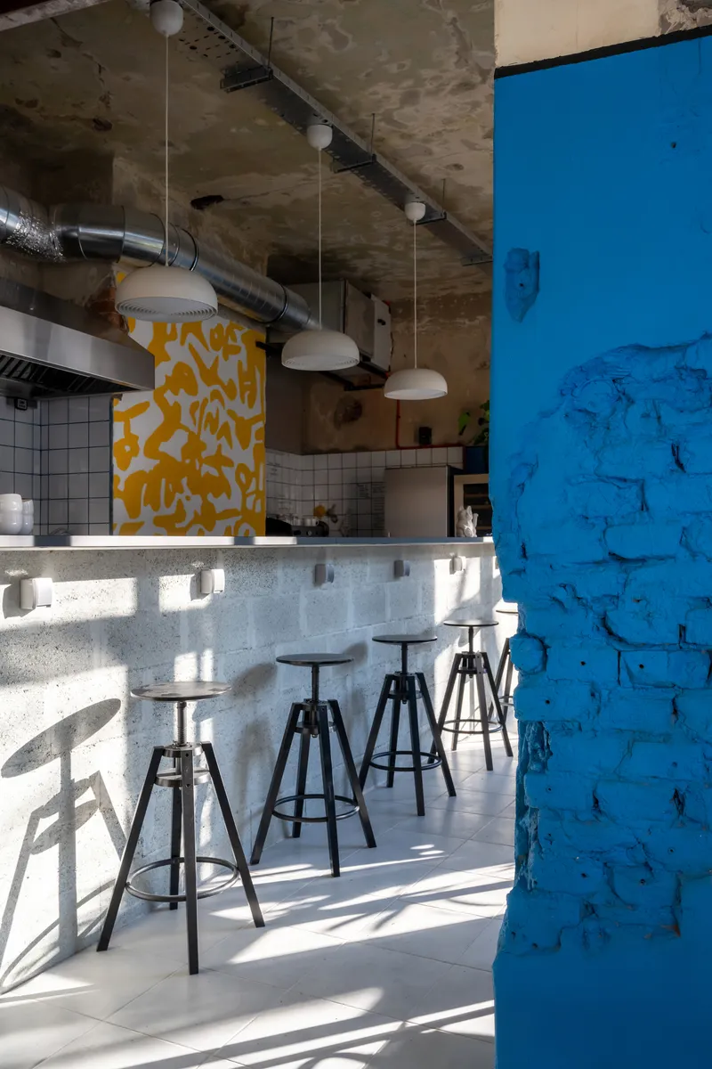 Service counter with adjustable stools beneath exposed concrete ceiling and pendant lights in afternoon sun