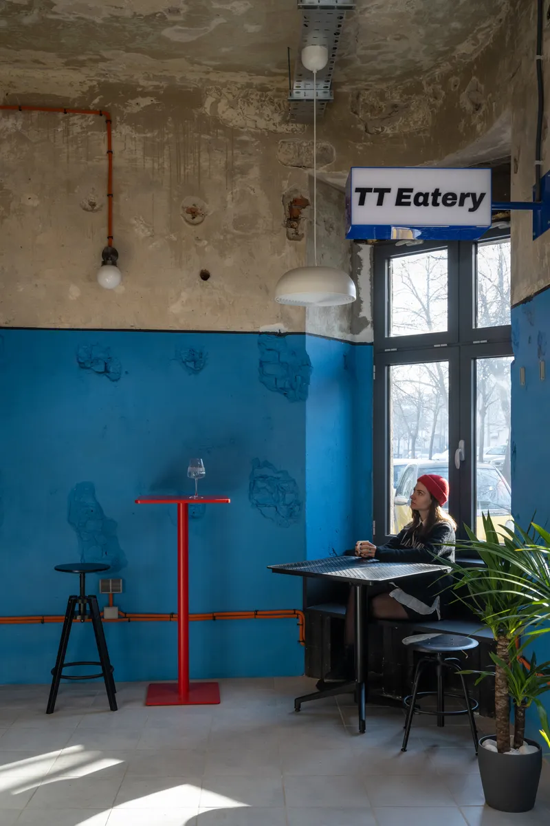 Seated figure at a table beneath weathered concrete ceiling with exposed conduit and pendant lighting