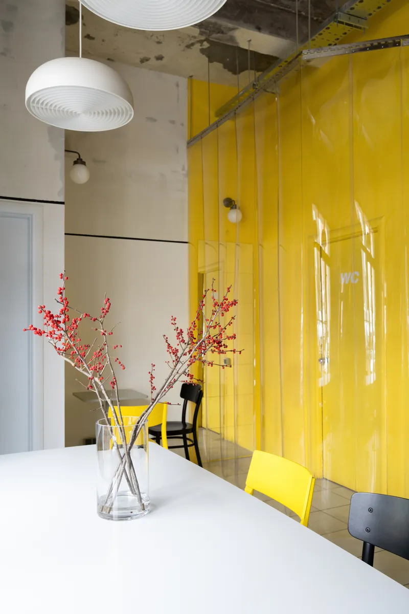 Glossy yellow glass partition wall reflecting window light beside a white table with red branches