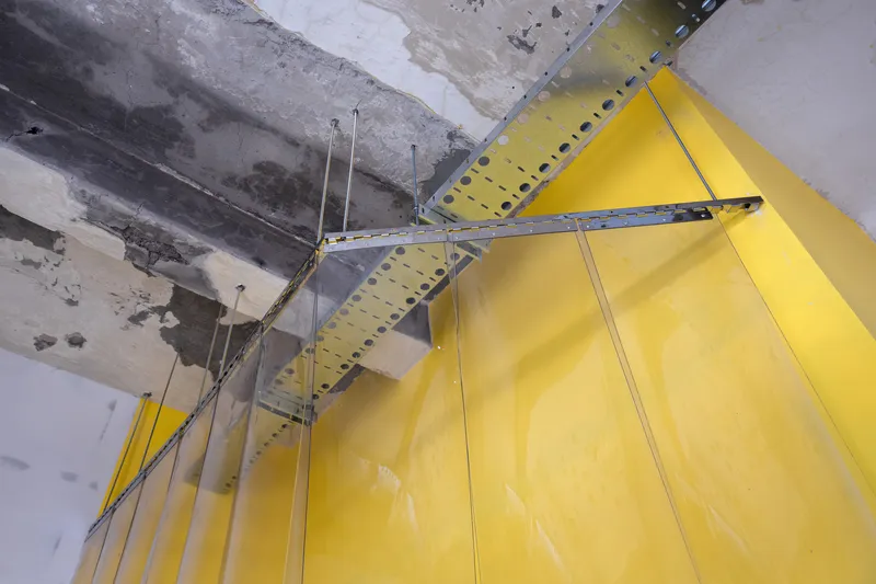 Yellow curved partition wall suspended from exposed concrete ceiling with metal brackets and rods