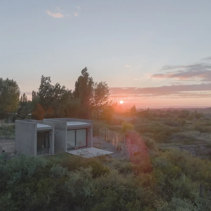 Concrete volumes with flat roofs nestled in scrubland vegetation at sunset