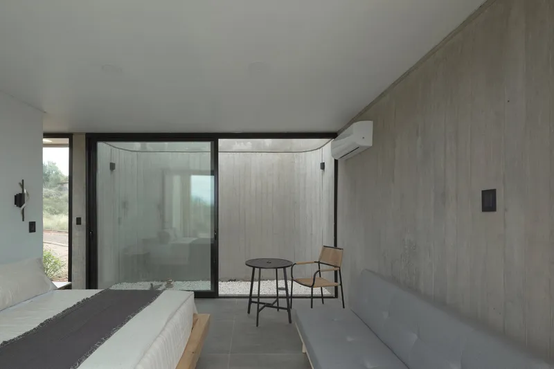 Bedroom with boardformed concrete walls and a glazed corner opening to a private courtyard