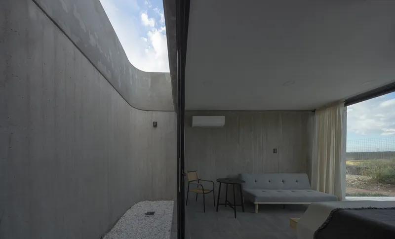 Bedroom interior opening to a private courtyard through floor-to-ceiling glass under an overcast sky