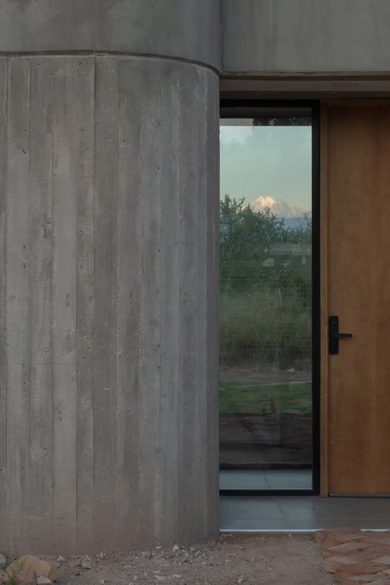 Curved concrete wall beside a timber door with a snow-capped mountain visible at dusk