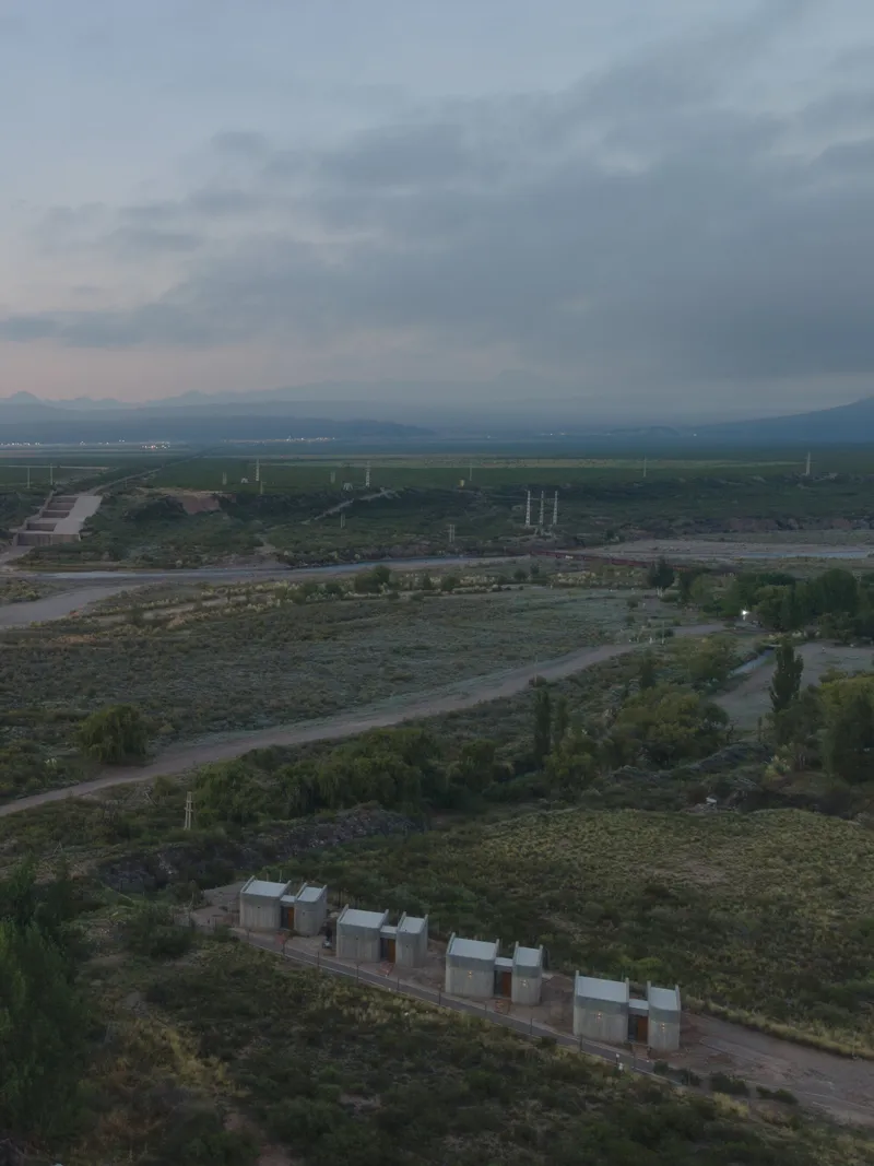 Aerial view of concrete volumes aligned in scrubland at dusk with distant fields and mountains