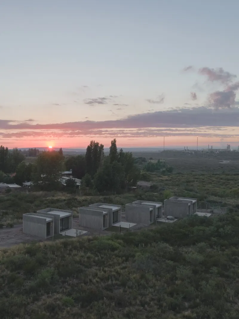 Cluster of concrete volumes with dark window openings in scrubland at sunrise