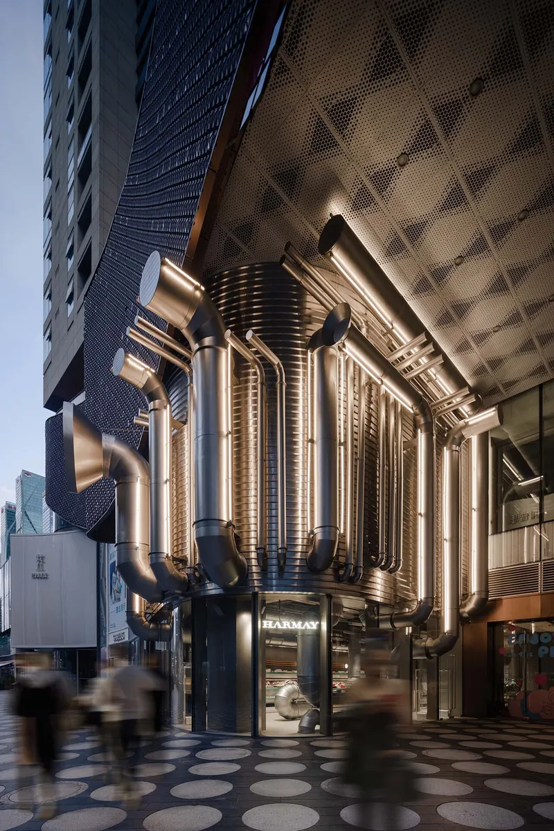 The image showcases a modern commercial building with a striking facade featuring a cylindrical structure adorned with numerous metal pipes. The design incorpor