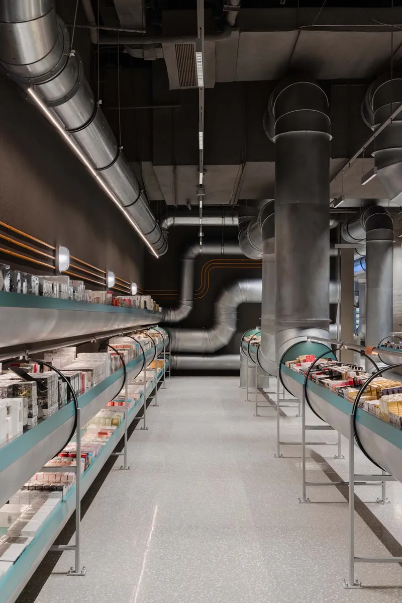 Retail interior with exposed metal ductwork threading between turquoise display shelves and cylindrical columns