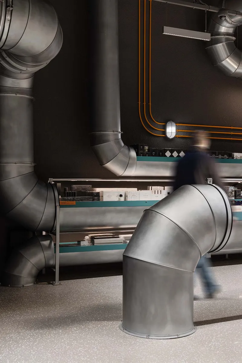 Close-up of sculptural elbow joints in the exposed ductwork above turquoise shelving units
