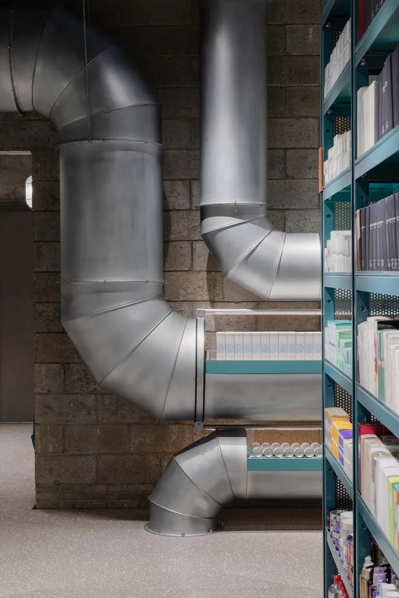 Exposed galvanized steel ductwork snaking through a stone block interior with teal shelving units