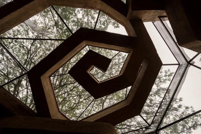 Upward view of spiraling hexagonal concrete skylight framed by tree canopy visible through glass