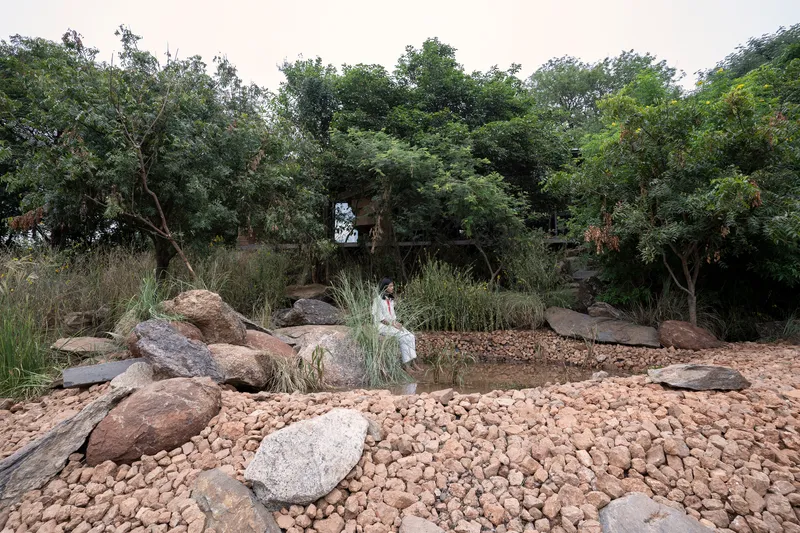 Natural pond surrounded by boulders and pebble beach with a figure wading in shallow water