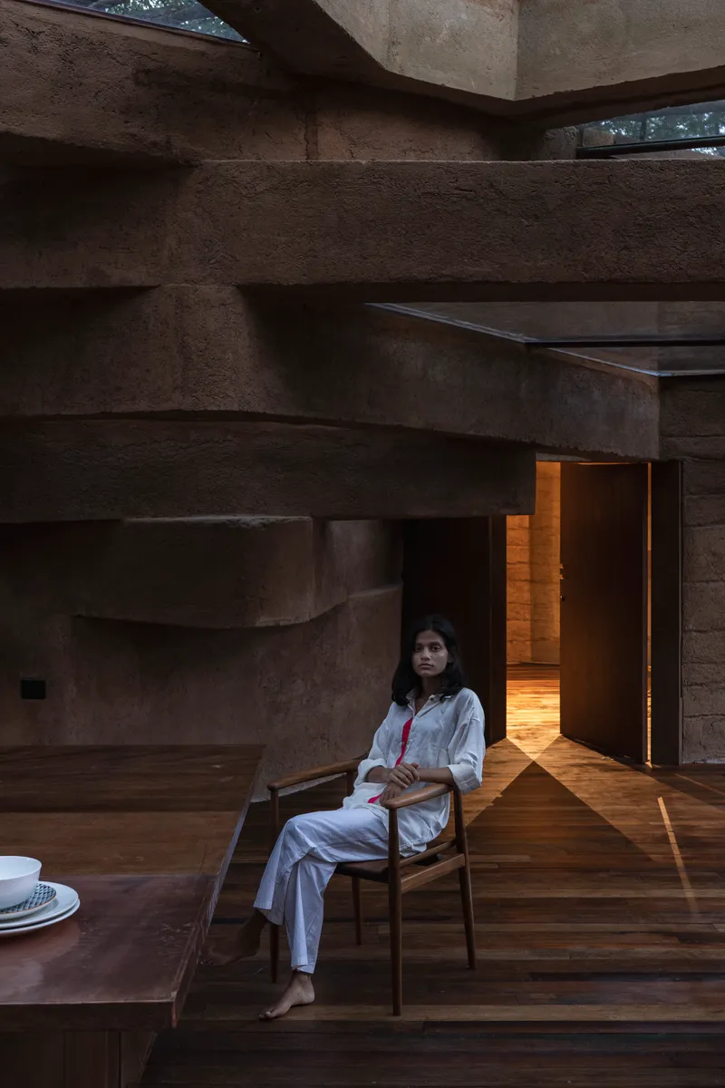 Layered earthen walls and timber flooring with a seated figure illuminated by warm afternoon light