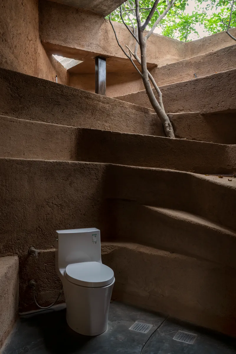 Bathroom with terraced earthen walls and skylight opening revealing tree branches above