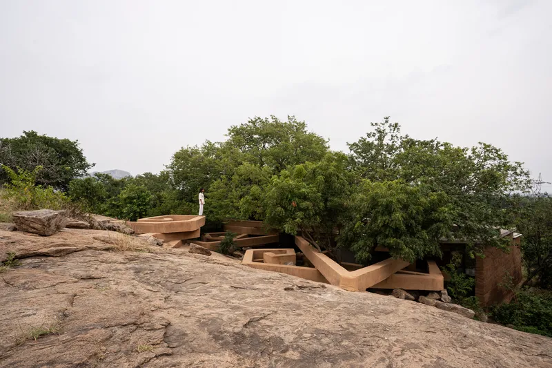 Exterior view of the layered rammed earth roof emerging from rocky terrain under an overcast sky