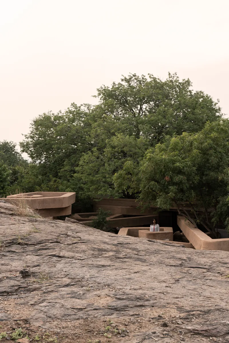 Two figures on the rocky landscape beside the layered rammed earth volumes nestled among mature trees