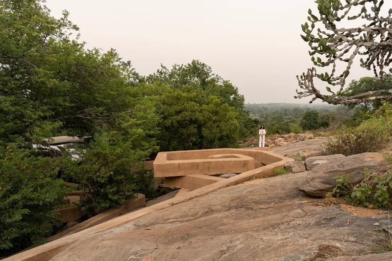 Curving concrete volumes rising from an exposed granite outcrop among dense tree cover